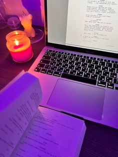 an open laptop computer sitting on top of a wooden desk next to a lit candle