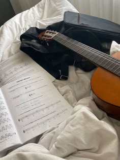 an acoustic guitar and sheet music on a bed