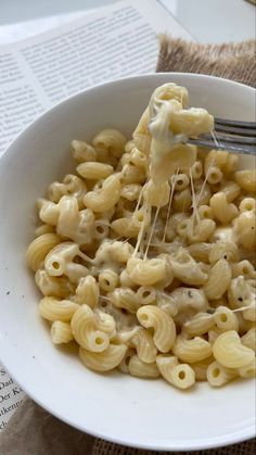 a white bowl filled with macaroni and cheese on top of a table next to an open book