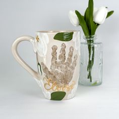 a coffee cup with a hand print on it next to a vase filled with tulips