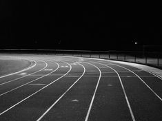 a black and white photo of a running track at night with the lights turned on