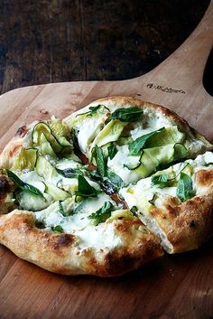 a pizza with zucchini, cheese and spinach on a wooden cutting board