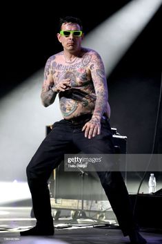 tattooed man sitting on stage with his arms crossed and legs crossed, in front of spotlights