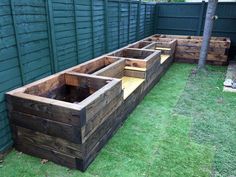 wooden planters sitting in the grass next to a fence and green wall behind them