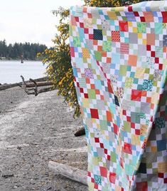 a patchwork quilt sitting on top of a wooden bench next to a lake and trees