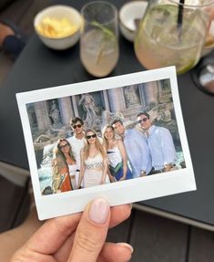 a person holding up a polaroid photo in front of some drinks