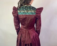 "An extravagant set from the Victorian era, this 1800's set will have you dripping in finery! The bodice is constructed of ox blood red silk with a the front and back yoke decorated with a black lace overlay on top of striped silk of cream and sky blue. The bodice features the classic pigeon bust shape aided by vertical knife pleats which also conceal the eleven button fastening, shoulder ruffles, and beautiful arced seaming on the back leading to a tail feather peplum. The silk skirt has a ruff Red Victorian Dress For Formal Occasions, Traditional Fitted Victorian Dress For Costume Party, Traditional Fitted Victorian Costume Dress, Fitted Red Victorian Dress For Evening, Formal Fitted Silk Victorian Dress, Traditional Victorian Costume Dress, Formal Fitted Victorian Dress With Historical Design, Traditional Fitted Long Sleeve Victorian Dress, Red Vintage Victorian Dress For Formal Occasions