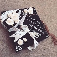 a graduation cap decorated with white roses and ribbon on the ground next to a ruler