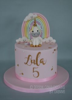 a pink cake with a unicorn on top and rainbows in the background that says lula 5