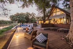 an outdoor deck with chairs and tables next to the water at sunset or sunrise time