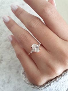 a woman's hand with a diamond ring on top of her finger and white nails