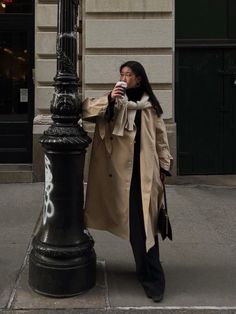 a woman standing next to a street light holding a cup in her hand and looking at the camera