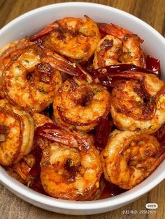 a white bowl filled with cooked shrimp on top of a wooden table