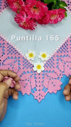 two hands are crocheting the edges of a doily with flowers on it