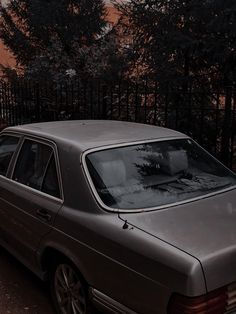 a car is parked in front of a fence and trees at sunset with the sun going down