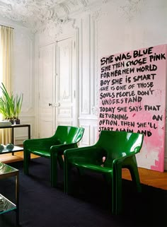 two green chairs sitting in front of a painting on the wall next to a coffee table