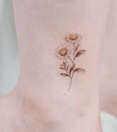 a woman's ankle with two daisies tattooed on the bottom of her foot