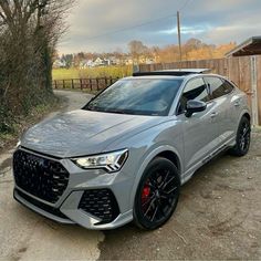 a grey audi suv parked in front of a wooden fence and building on the other side