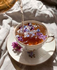 tea being poured into a cup with purple flowers on the saucer next to it