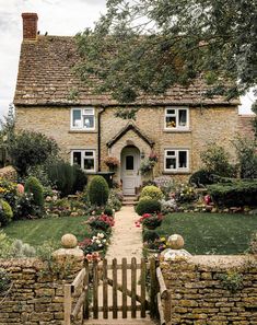 a stone house with flowers in the front yard and steps leading up to it's entrance