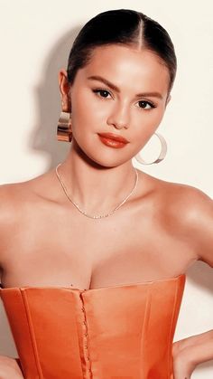 a woman in an orange dress posing with her hands on her hips and wearing large hoop earrings