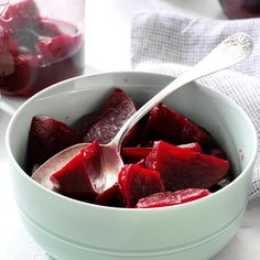 a white bowl filled with beets on top of a table next to a spoon