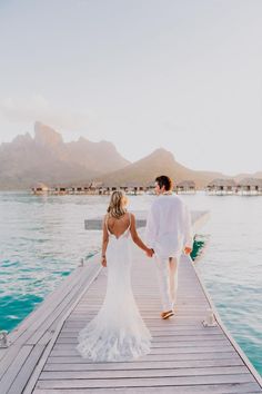 a bride and groom walking on a dock holding hands