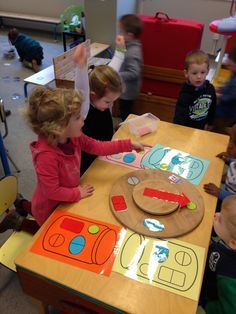 several children are sitting at a table playing with paper plates and magnets on it