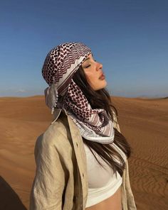 a woman standing in the desert wearing a scarf and head wrap on top of her head