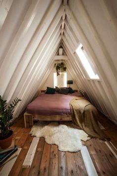 an attic bedroom with white walls and wood flooring is furnished with natural materials such as bedding, rugs and pillows