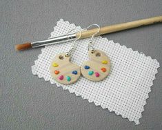 a pair of wooden earrings sitting on top of a doily next to a paintbrush