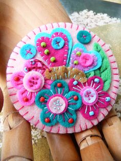 a close up of a pink and blue flower brooch on a person's hand