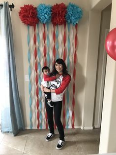 a woman holding a child in front of a wall decorated with red, white and blue streamers