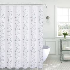 a white shower curtain with blue flowers on it in a bathroom next to a window