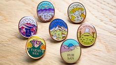 six pin badges sitting on top of a wooden table with mountains and clouds in the background