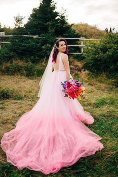 a woman in a long pink dress holding a bouquet and posing for the camera on her wedding day