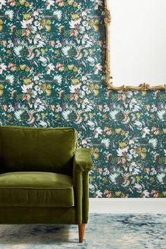 a green chair in front of a floral wallpaper with a gold framed mirror on it