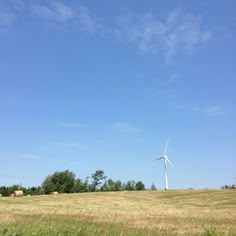 a wind turbine is in the middle of a field with hay and trees behind it