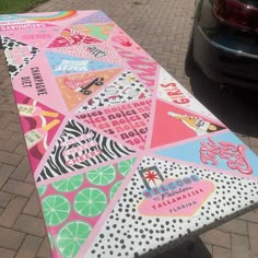 a large colorful surfboard sitting on top of a brick sidewalk next to a parked car