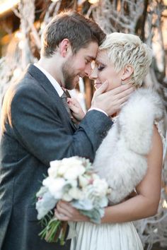 a bride and groom embracing each other in front of some snow - covered trees at their wedding