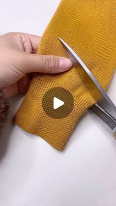 someone using scissors to cut the fabric off of a yellow sweater with white stitchs