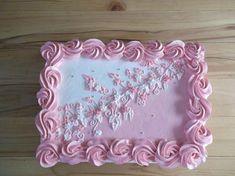 a pink cake with white frosting and flowers on the top is sitting on a wooden table