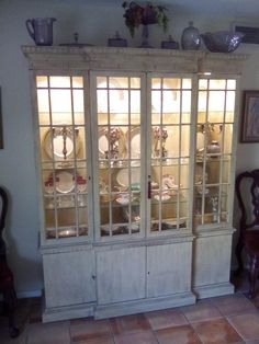 an old china cabinet with glass doors and plates on the top, sitting in a living room