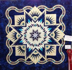 a blue and white quilt on display in a room with red ribbon around the edges