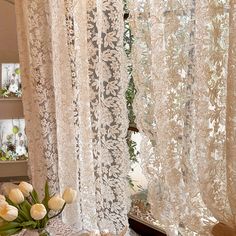 white tulips sit on a table in front of a window with lace curtains