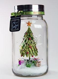 a christmas tree in a glass jar with snow on the bottom and writing underneath it