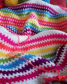 a multicolored crocheted blanket with yarn on it and balls of thread