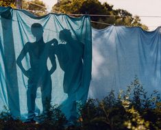 two people standing in front of some clothes hanging on a line with trees and bushes behind them