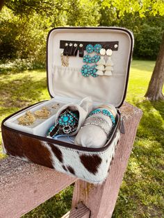 an open suitcase filled with jewelry sitting on top of a wooden bench next to trees