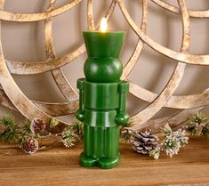 a green candle holder sitting on top of a wooden table next to some pine cones